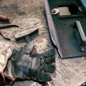 Various quality welding tools, including a mask, gloves, hammer, and pliers, all neatly laid out on a workbench.