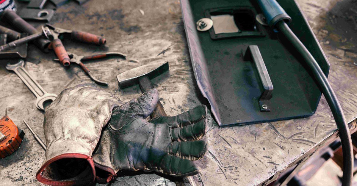 Various quality welding tools, including a mask, gloves, hammer, and pliers, all neatly laid out on a workbench.