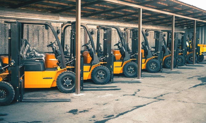 Eight yellow forklifts in like-new condition parked diagonally under a tin-roof shelter in a concrete lot.