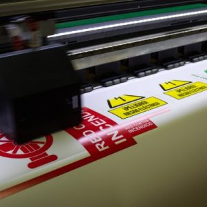 A wide-format printer is producing a large-scale image of various signs in different bright and vivid colors.