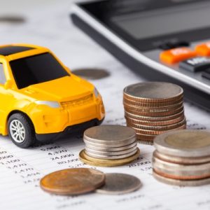 A yellow toy car sitting next to three stacks of various coins and a calculator on a printed spreadsheet.