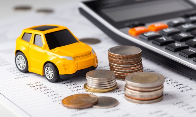 A yellow toy car sitting next to three stacks of various coins and a calculator on a printed spreadsheet.