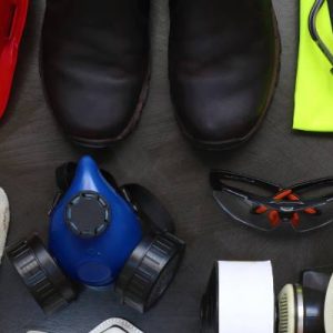 PPE laid out against a black background. There's a hard hat, boots, earmuffs, ear plugs, gloves, masks, and safety glasses.