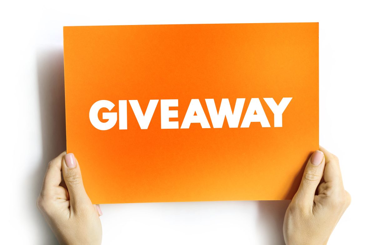 A close-up of a person holding an orange card featuring the word "giveaway" in bold, eye-catching typography.