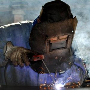 A welder in full protective gear, focused on the welding process, with bright sparks illuminating the workspace around them.
