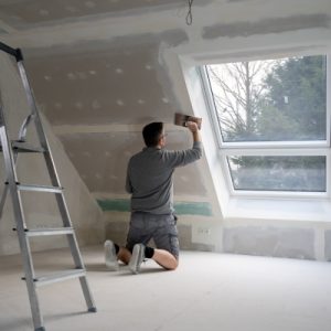 A man applying plaster to drywall in a residential home, focusing on achieving a smooth finish before painting.