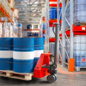 A pallet jack with a pallet and barrels of chemicals on it, in a warehouse setting with intermediate bulk containers.