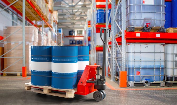 A pallet jack with a pallet and barrels of chemicals on it, in a warehouse setting with intermediate bulk containers.
