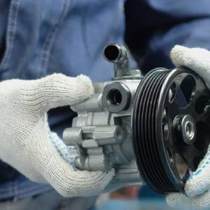 An individual is wearing a denim shirt and pants and white gloves. He is holding both ends of a metal pump.