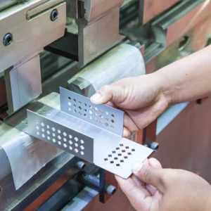 A manufacturer placing a metal component into a metal stamping machine. The metal part has punched holes throughout.