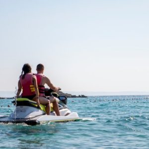 A couple rides on a jet ski on the ocean. The waves go on for a long time while the sky is clear and free of clouds.