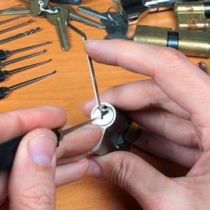A locksmith sitting at their workstation with a set of lock picking tools. They're practicing on a lock off the door.