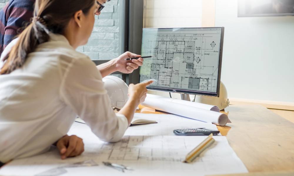A professional architect designer team working and looking at a computer, discussing a building plan design project.