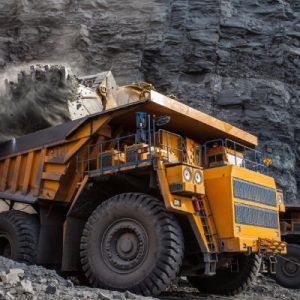 A large yellow mining truck in a quarry is loading a massive amount of coal and coal dust into the rear compartment.