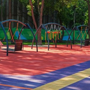 A large playground with inclusive-specific play structures. The ground is red and blue soft-landing rubber.