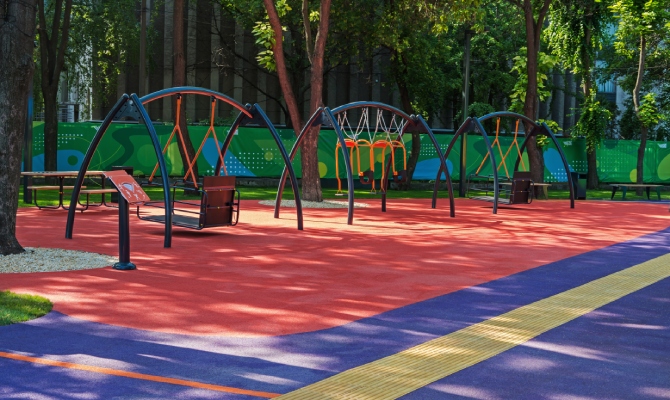 A large playground with inclusive-specific play structures. The ground is red and blue soft-landing rubber.