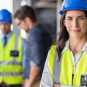 A female contractor standing in the foreground with her arms crossed and three males blurred out in the background.