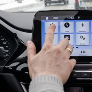 A daily commuter in their car managing their infotainment system with their index finger. The system is on the main menu.