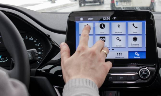 A daily commuter in their car managing their infotainment system with their index finger. The system is on the main menu.