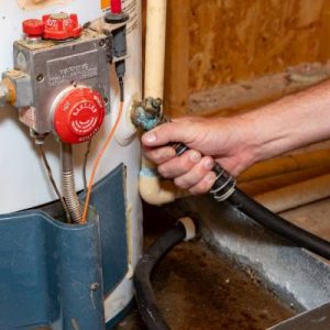 Someone holding onto a pipe that comes off their home water heater. The connection has corrosion on the knob.
