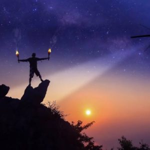 A helicopter shining a light toward the ground in the evening. A person on the ground is holding up a fire signal.