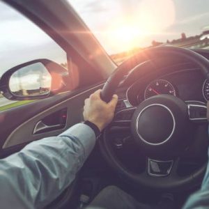 An over-the-shoulder view of a driver handling a modern car on the highway with both hands on the steering wheel.