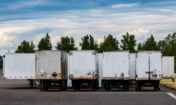 Several semi-tractor trailers stand next to each other in a parking lot. Most feature a white color, while one is silver.