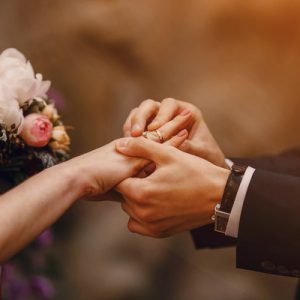 A bride and groom at their wedding ceremony exchanging vows and rings. The groom is placing the ring on her finger.