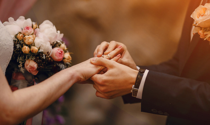 A bride and groom at their wedding ceremony exchanging vows and rings. The groom is placing the ring on her finger.