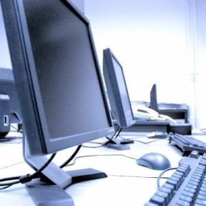 A close up view of a desk and the different black monitors, keyboards, and computer mouses sitting on top of it.