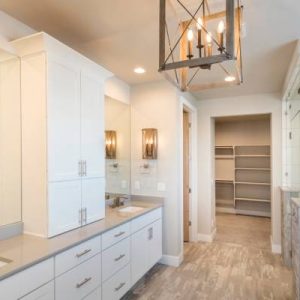 A newly renovated bathroom with white cabinets and a quartz countertop. There's silver hardware and farmhouse lighting.