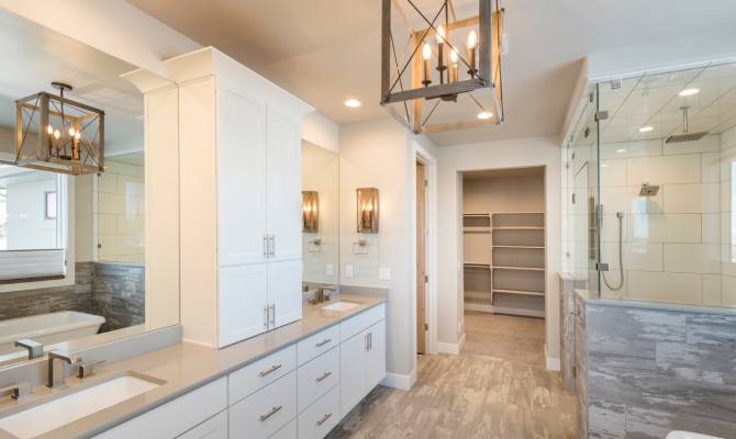 A newly renovated bathroom with white cabinets and a quartz countertop. There's silver hardware and farmhouse lighting.