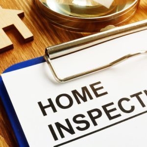 A close-up of a clipboard with a piece of paper attached to it that says "HOME INSPECTION" in big block letters.
