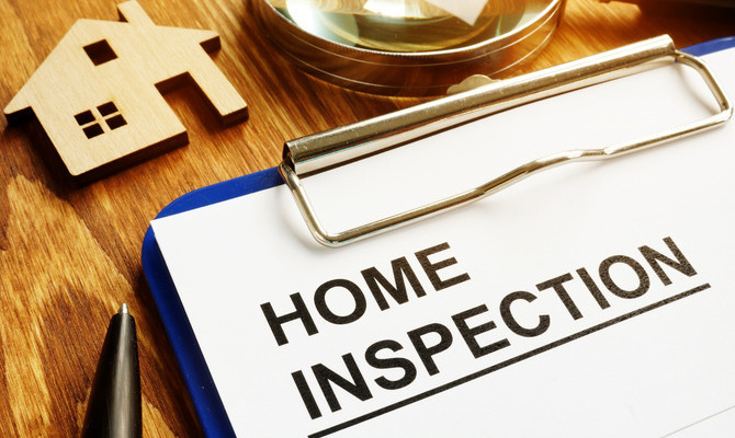A close-up of a clipboard with a piece of paper attached to it that says "HOME INSPECTION" in big block letters.
