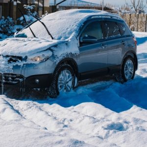 An SUV with its wipers raised is parked in the front yard of a home, completely covered in snow and icicles.