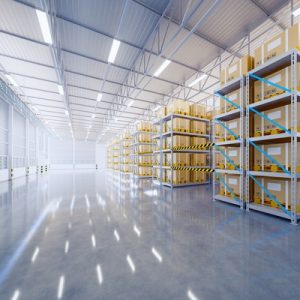 A large warehouse contains a gray, shiny floor and silver vertical storage units with large cardboard boxes.