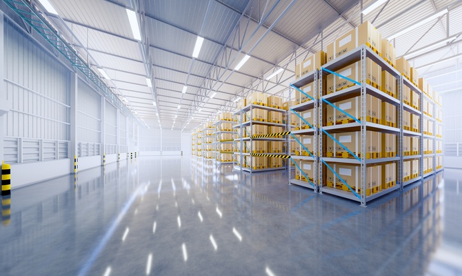A large warehouse contains a gray, shiny floor and silver vertical storage units with large cardboard boxes.