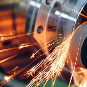 A close-up of sparks flying as a machine tool grinds against a metal surface. The sparks leave trails in the air.