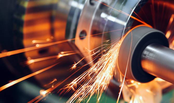 A close-up of sparks flying as a machine tool grinds against a metal surface. The sparks leave trails in the air.
