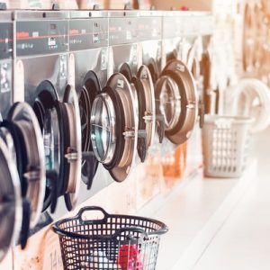 Several laundry baskets sit in front of a row of laundry machines in a laundromat. The machine doors are open.