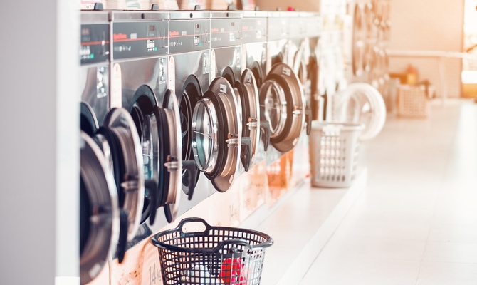 Several laundry baskets sit in front of a row of laundry machines in a laundromat. The machine doors are open.