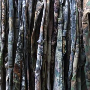 A close-up of a large collection of various types of military camouflage pants hung on a rack together.