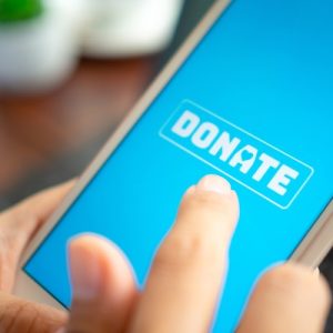 A close-up of an individual's finger hovering over a blue smartphone screen with a white button that says "Donate."