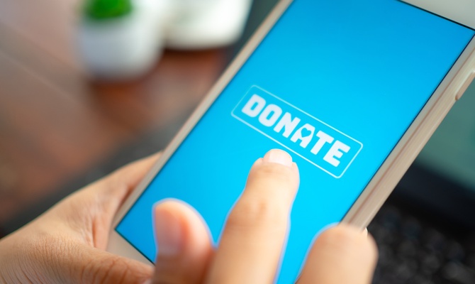 A close-up of an individual's finger hovering over a blue smartphone screen with a white button that says "Donate."
