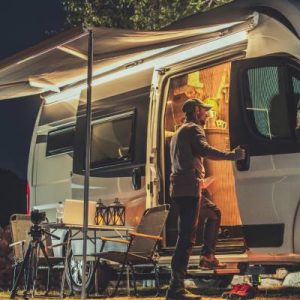 A man looking inside the side door of his campervan with an awning coming out of the van and a small table resting outside.
