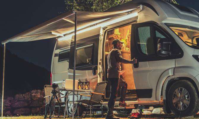 A man looking inside the side door of his campervan with an awning coming out of the van and a small table resting outside.