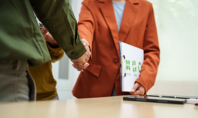 Two business professionals shaking hands after agreeing to a waste contingency plan. One person has a clipboard.