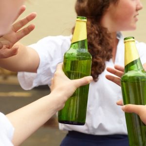 A teenage student turns down two bottles of alcohol being held out to her by two other people by holding up her hands.