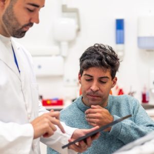 A healthcare provider standing at the bedside of a male patient. They're reading a clipboard together.