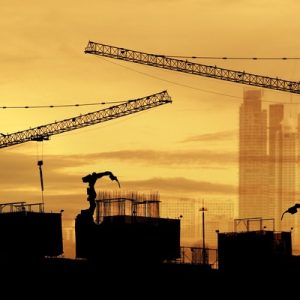 The silhouette of a construction site against a yellow sky. Several cranes are visible in silhouette.